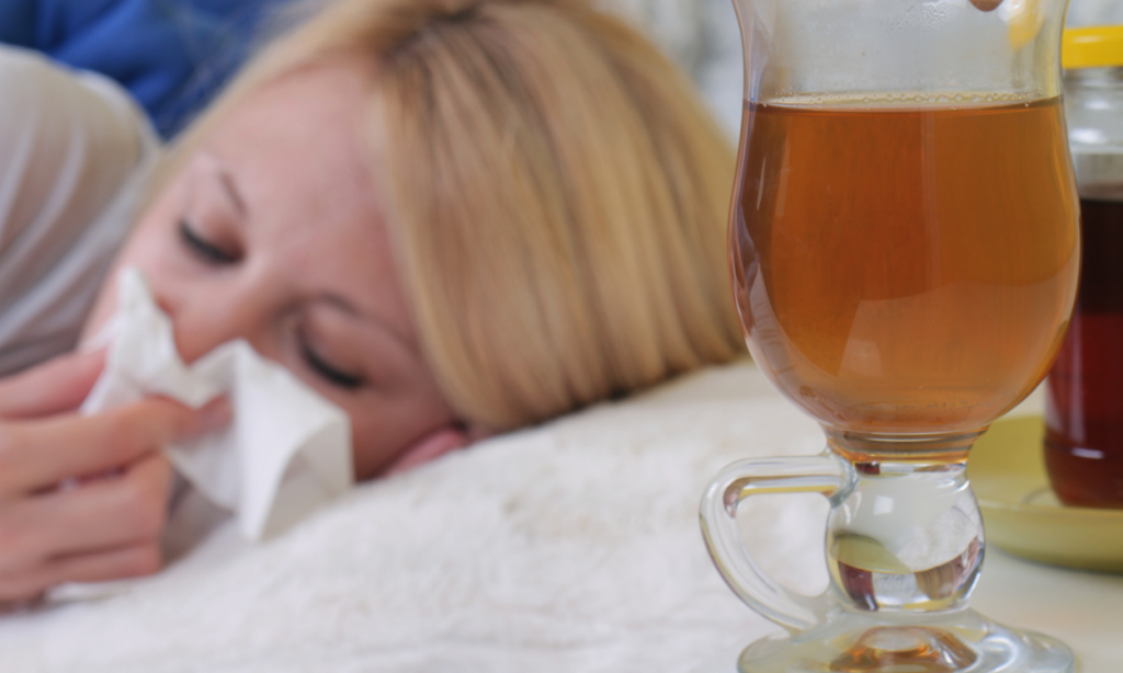 Žena leži u krevetu i briše nos, pored je stočić sa čajem